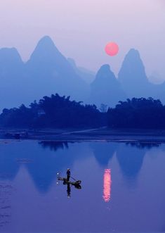 a person on a small boat in the water with mountains in the backgroud