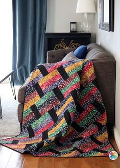 a living room with a couch covered in a multicolored quilt next to a lamp