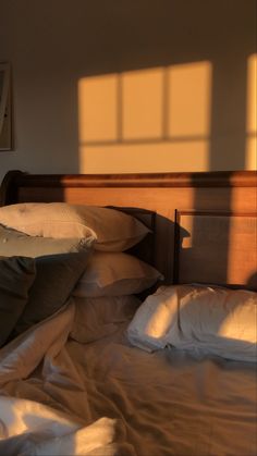 an unmade bed with white sheets and pillows in the morning sun shining on it