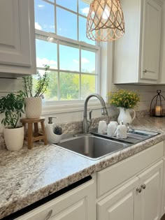 a kitchen sink under a window next to a counter top with flowers in vases