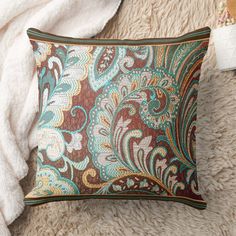 a brown and blue decorative pillow sitting on top of a white rug next to a blanket