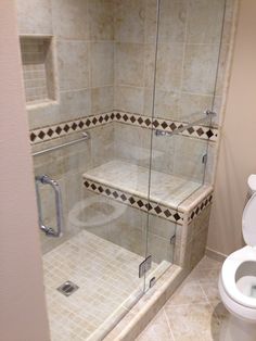 a white toilet sitting next to a walk in shower with glass doors on both sides