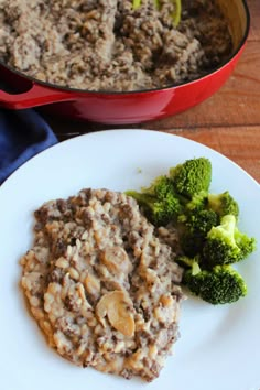 a white plate topped with oatmeal next to a red pot filled with broccoli