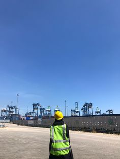 a man in yellow safety vest standing next to an empty parking lot with lots of cranes behind him