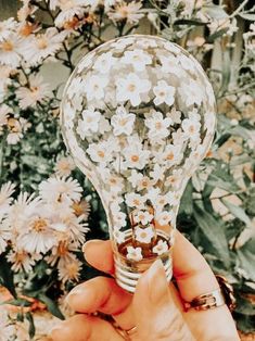 a person holding up a light bulb with flowers on it in front of some wildflowers