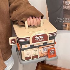 a person is holding a small suitcase shaped like a coffee machine