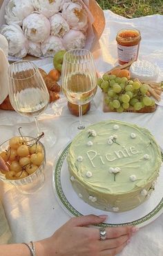 a table topped with a cake covered in frosting next to wine glasses and fruit