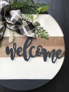 a welcome sign is hanging on a door with greenery and ribbon around the word