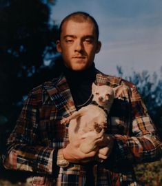 a man holding two puppies in his arms and looking at the camera while standing outside