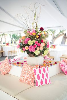 a vase filled with pink and white flowers on top of a table covered in pillows