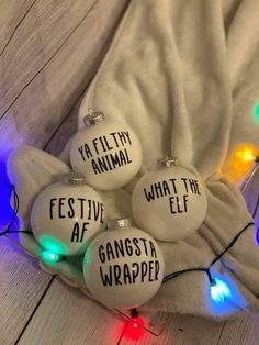 five white glass ornaments with words on them sitting on a blanket next to christmas lights