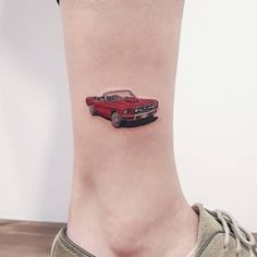 a small red car tattoo on the right side of the ankle, with an arrow in the center