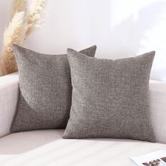 two gray pillows sitting on top of a white couch