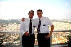 two men standing next to each other in front of a city view from a high rise