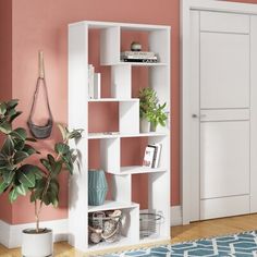 a white bookcase in a living room next to a pink wall and potted plant