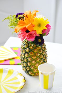 a pineapple vase filled with colorful flowers next to a cup and plate on a table