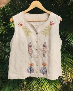 a white shirt with fish on it hanging from a wooden hanger in front of palm trees