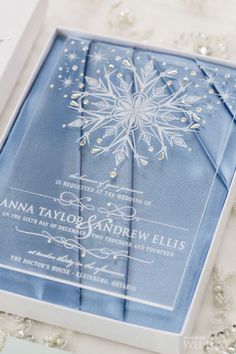 a blue and white wedding card in a box on a lace tablecloth with snowflakes