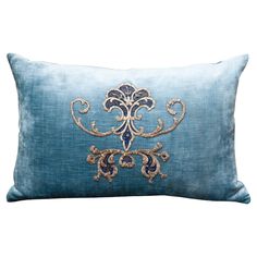 a blue and gold pillow with an embroidered design on the front, sitting against a white background