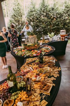 a table full of different types of food and wine on it with people standing around