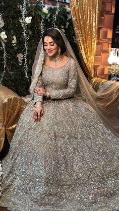 a woman in a wedding dress sitting on a bed with gold sequins and flowers