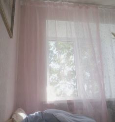 a bed sitting under a window next to a pink curtain and pillow on top of it