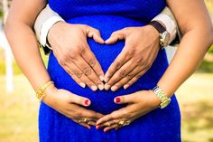 a pregnant woman holding her husband's belly in the shape of a heart with both hands