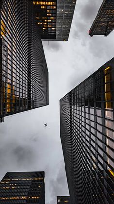 looking up at skyscrapers from the ground with a plane flying in the sky above them