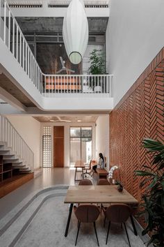 a person sitting at a wooden table in a room with stairs and plants on the floor