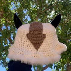 a crocheted hat with an arrow on it hanging from a tree in front of some leaves