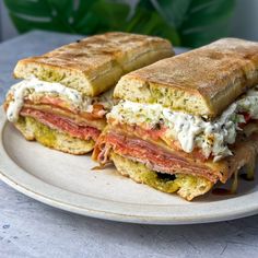 two halves of a sandwich sitting on top of a white plate next to a green plant