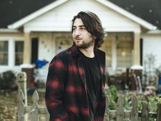 a man standing in front of a house wearing a red and black checkered shirt