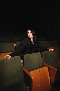 a woman sitting in an empty auditorium with her hands on the back of some chairs