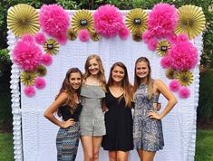 three girls standing in front of a white backdrop with pink and gold pom poms