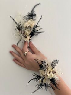 two hands are shown holding flowers on the palm of someone's hand, both with black and white feathers