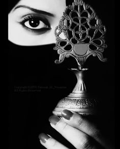 a woman is hiding her face behind a metal vase with an ornate decoration on it