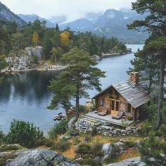 a small cabin sits on the edge of a lake surrounded by trees and rocks with mountains in the background