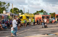 a group of people standing around food trucks in a parking lot next to each other