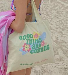 a woman standing on the beach with a tote bag in front of her back