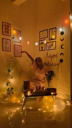 a woman sitting on top of a table in front of balloons and lights with the words happy birthday hanging above her