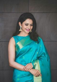 a woman in a blue and green sari with her hands on her hips, smiling