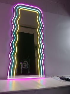 an illuminated mirror in the shape of a wave with neon lights on it's sides