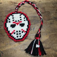 a cross - stitch skull ornament hanging on a wooden table with a tassel