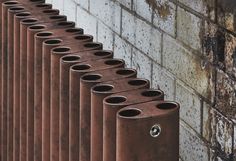 a row of rusted metal pipes next to a brick wall