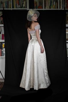 a woman in a white dress and hat standing next to a book shelf filled with books