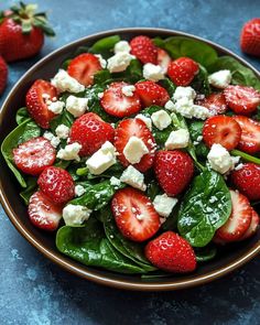 a salad with spinach, strawberries and feta cheese in a brown bowl