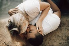 a man and woman laying on the ground kissing each other with their heads close to one another