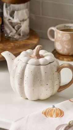 a ceramic teapot with a white pumpkin on it sitting on a counter next to cups and saucers