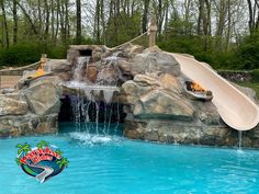 a water slide in the middle of a swimming pool with rocks and trees around it