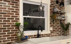 a kitchen with brick walls and white cabinets, an island sink and black faucet